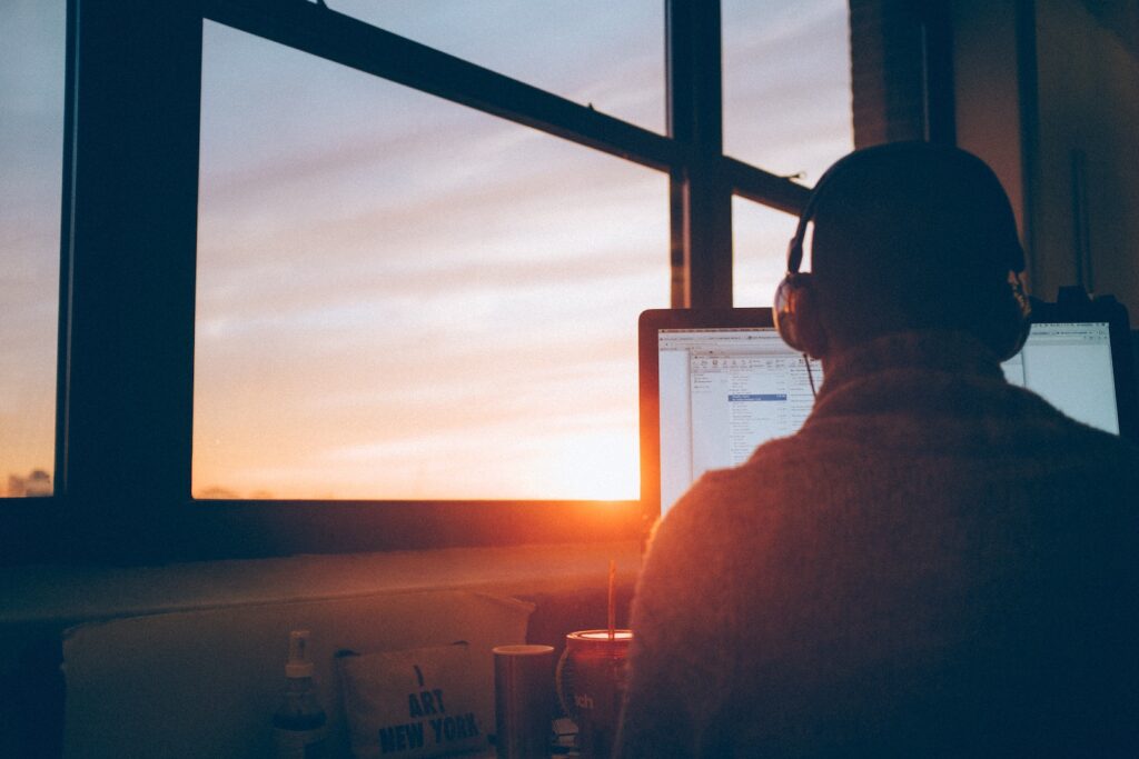 man sits in front of computer with sunset in background